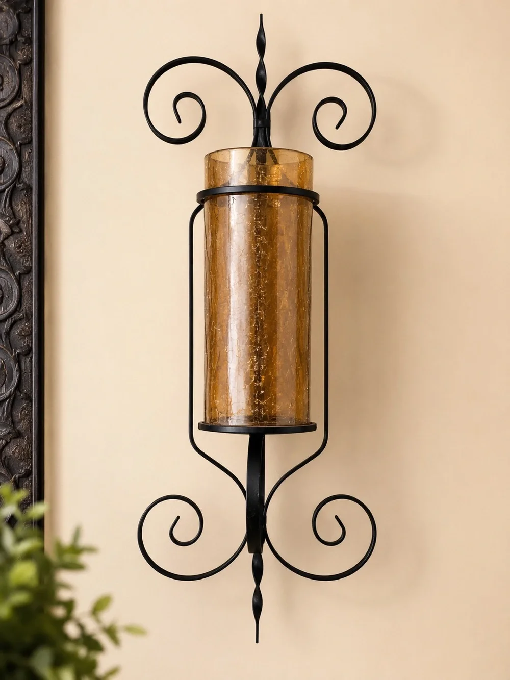Black wrought iron wall sconce with amber glass cylinder and swirling scrollwork